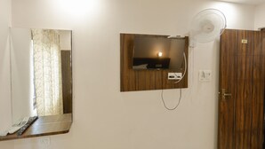 Un baño con puerta de madera, un espejo con marco de madera, un ventilador de pared y un perchero para toallas.