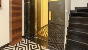 Un ascensor moderno con superficie reflectante, suelo estampado y una escalera con peldaños oscuros.
