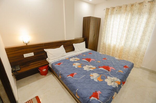 A bedroom with a wooden headboard, a floral bedspread, a red bucket, and a curtain with a tree pattern. - SSR STAY (Amritsar)