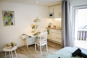 Een kleine keuken met witte kasten, een magnetron, en een eethoek met een witte tafel en stoel.