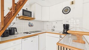 A compact kitchen with white cabinets, a wooden staircase, a microwave, a coffee maker, and a clock on the wall. - Apartment with Loggia and Sea View for 4 (Saint-Hilaire-de-Riez)