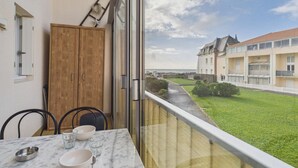 A balcony with a table, chairs, and a view of a coastal building. - Apartment with Loggia and Sea View for 4 (Saint-Hilaire-de-Riez)