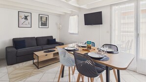 A modern living room with a sofa, dining table, chairs, and a TV mounted on the wall. - Apartment with Loggia and Sea View for 4 (Saint-Hilaire-de-Riez)