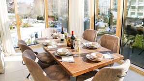 Un comedor con una larga mesa de madera dispuesta para seis personas, ventanas amplias y vistas a un paisaje nevado.