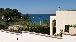 A coastal view with a clear sky, a pathway leading to a building with an arched entrance, and a bench area with a view of the sea. - House Cà Luci 100 mt from the sea (Patù)