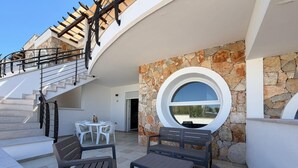 A modern outdoor patio with a stone wall, a circular window, and a staircase leading to an upper level. - House Cà Luci 100 mt from the sea (Patù)