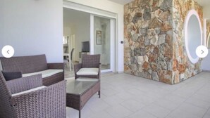 A modern living room with wicker furniture, a stone accent wall, and a glass door leading to a balcony. - House Cà Luci 100 mt from the sea (Patù)