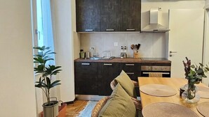 Een kleine keuken met donkere kastjes, een houten aanrecht en een eethoek met een tafel en stoelen.