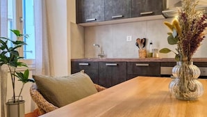 Een moderne keuken met donkere kastjes, een houten tafel en een vaas met gedroogde bloemen.