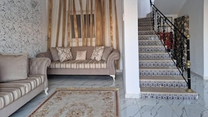 A living room with a sofa and a patterned rug, a staircase with patterned tiles, and a decorative railing. - Djerba 7 Exclusive Stay with Daily Homemade Brunch (Aghir)