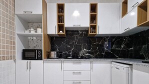 A modern kitchen with white cabinets, a black marble backsplash, and wooden shelves. - Djerba 7 Exclusive Stay with Daily Homemade Brunch (Aghir)