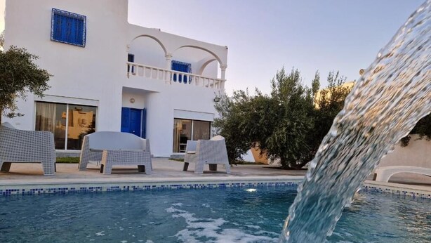 A pool with a waterfall feature, white building with blue accents, and outdoor seating. - Djerba 7 Exclusive Stay with Daily Homemade Brunch (Aghir)