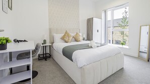 A modern bedroom with a large bed, a desk, and a window with a view of the outside. - Charming 3-bedroom House in Balsall Heath, Birmingham (Birmingham)