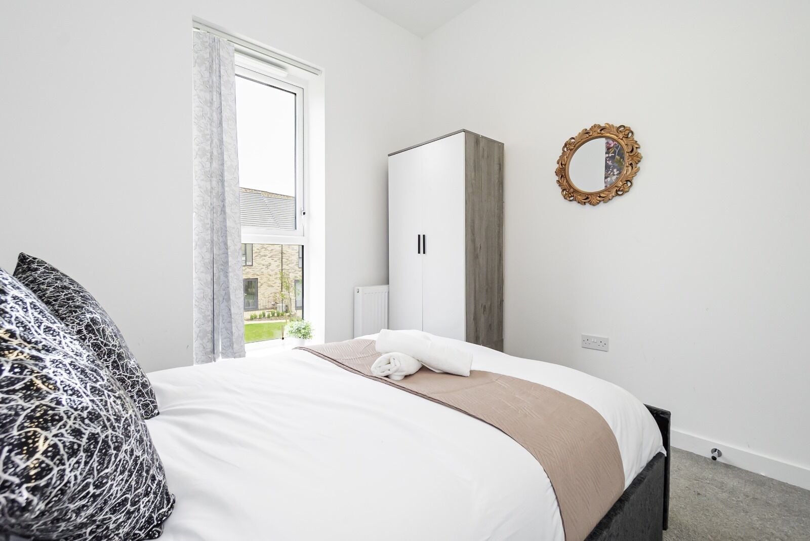 Een slaapkamer met een bed, een kledingkast, een spiegel en een raam met uitzicht op groen.
