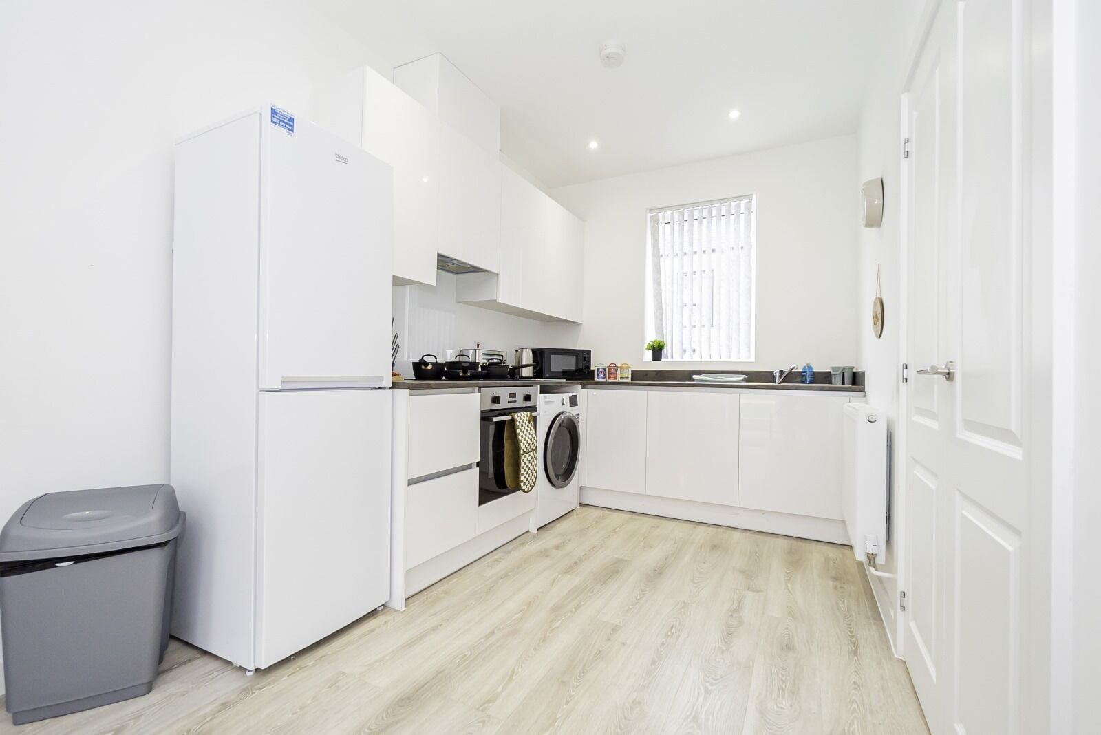 Une cuisine moderne avec des meubles blancs, un four encastré, un four à micro-ondes et un lave-linge.