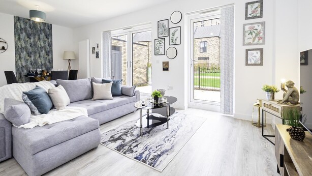 A modern living room with a grey sofa, a round coffee table, and a view of a brick building through large windows. - Charming 3-bedroom House in Balsall Heath, Birmingham (Birmingham)
