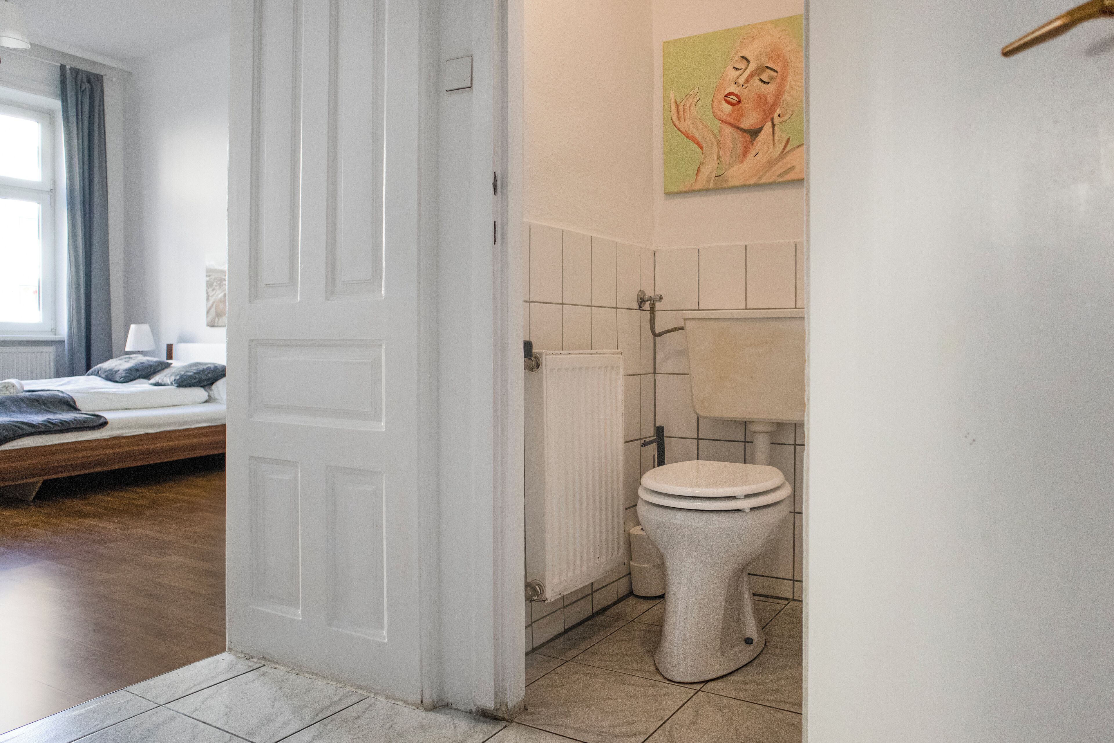 A bedroom with a bed, a bathroom with a toilet, and a door leading to another room.