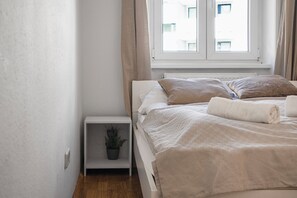 Ein Schlafzimmer mit einem Bett, einem Nachttisch mit Pflanze und einem Fenster mit Vorhängen.