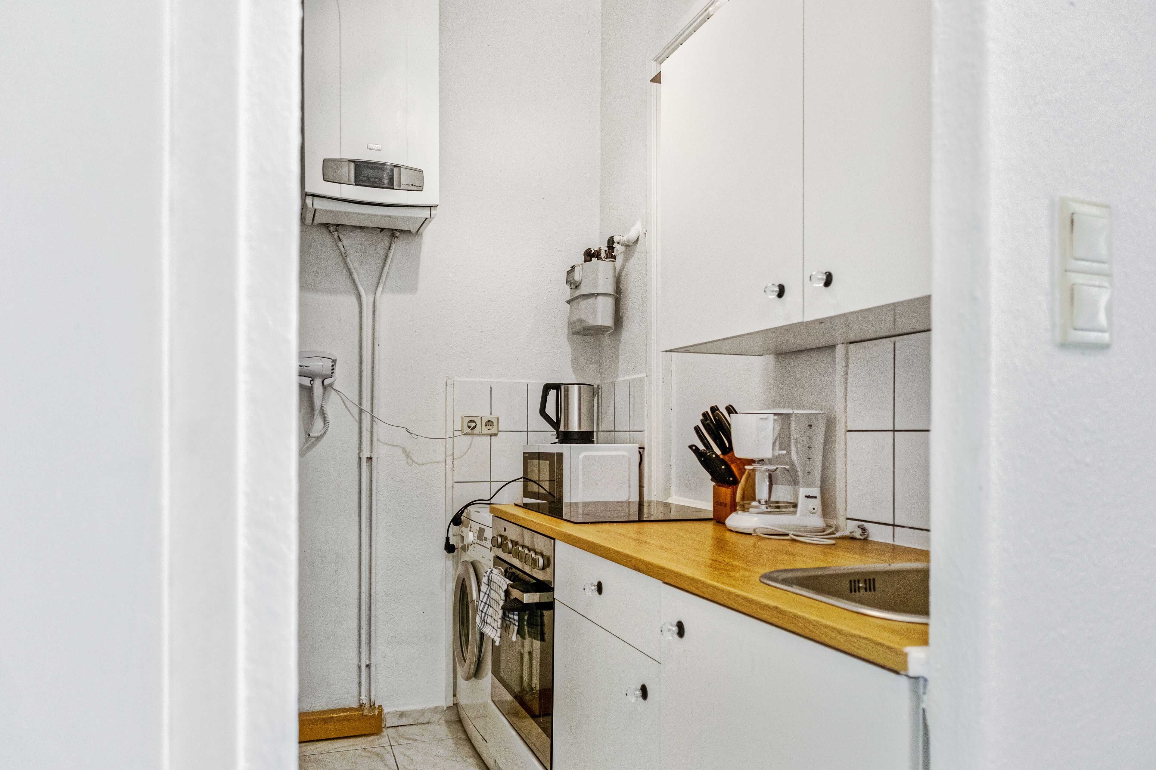 Een kleine keuken met witte kastjes, een houten aanrecht, een koffiezetapparaat en een wasmachine.