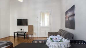 A modern living room with a sofa, a coffee table, a TV, and a door. - Comfy 2BR Apartment Long Stay Downtown (Vienna)