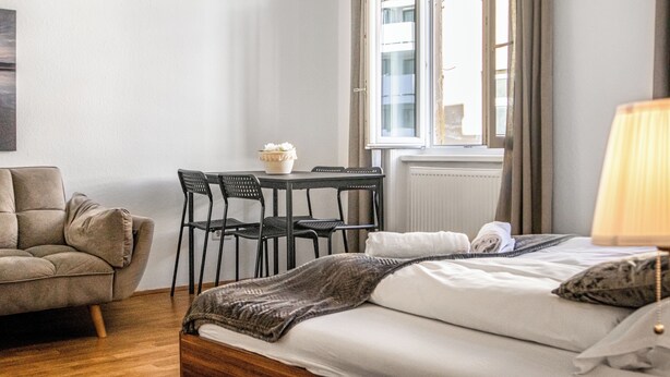 A bedroom with a bed, a chair, a table with chairs, and a window. - Comfy 2BR Apartment Long Stay Downtown (Vienna)