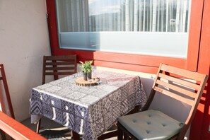 Una mesa con mantel estampado, dos sillas de madera, una planta pequeña en maceta y un ventanal con cortinas.