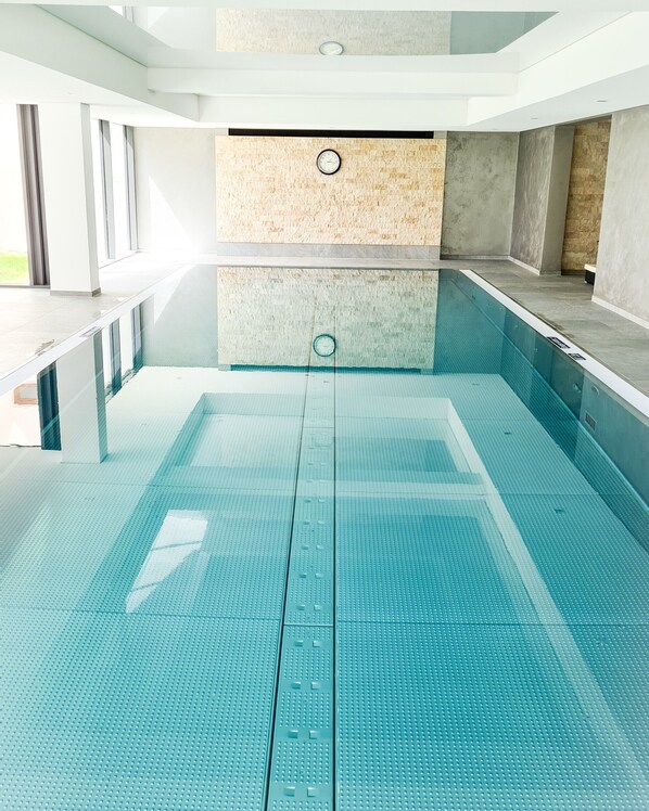 Una piscina interior con agua cristalina, suelo de baldosas y un reloj en la pared.