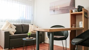 A modern living room with a sofa, a small round table with a plant, a wicker chair, and a wooden coffee table. - Apartment Nathalie – Wellness with Pool and Sauna (Schluchsee)
