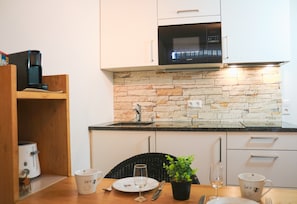 A kitchen with white cabinets, a stone backsplash, a microwave, and a dining table with a potted plant. - Apartment Nathalie – Wellness with Pool and Sauna (Schluchsee)