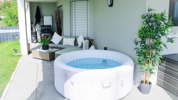 Un espace extérieur aménagé avec un jacuzzi, un canapé en osier, une petite table et un pot de fleurs.