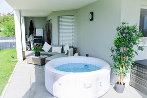 An outdoor hot tub area with a wicker sofa, a small table, and a potted plant. - Mountain View Deluxe Apartment with Private Whirlpool (Lottstetten)