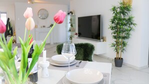 Un coin repas avec une table dressée pour deux personnes, une plante en pot et un téléviseur à écran plat fixé au mur.