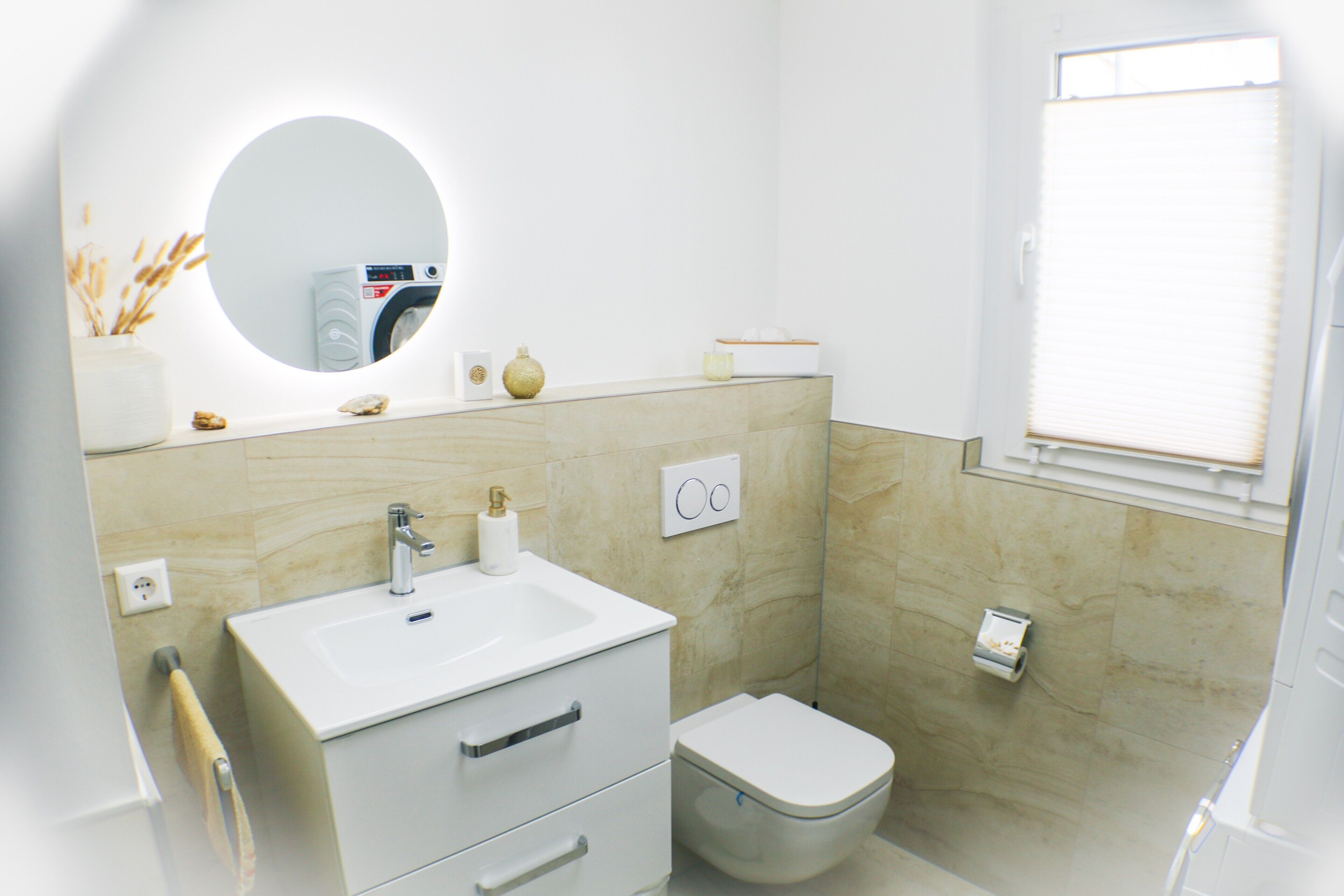 Un baño moderno con lavamanos, espejo, inodoro y ventana.