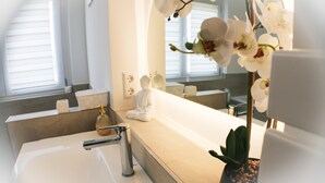 Une salle de bain avec un lavabo blanc, un miroir et une plante orchidée en pot.