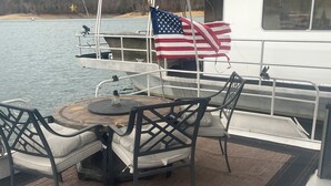 Ein Bootsdeck mit Tisch und Stühlen, eine amerikanische Flagge und Blick auf das Wasser.