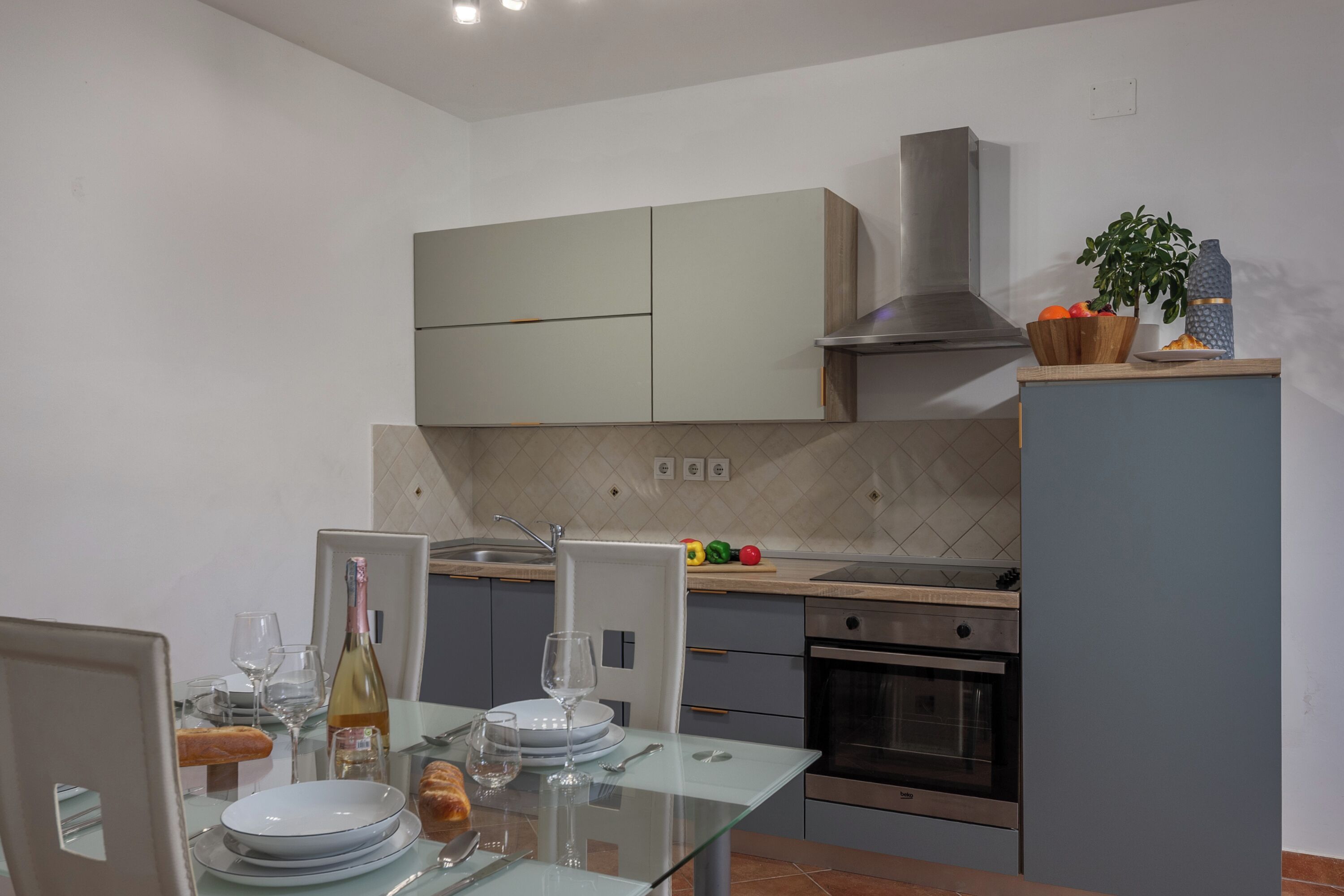Une cuisine moderne avec un coin repas, comprenant une table en verre, des appareils en acier inoxydable et une plante en pot.