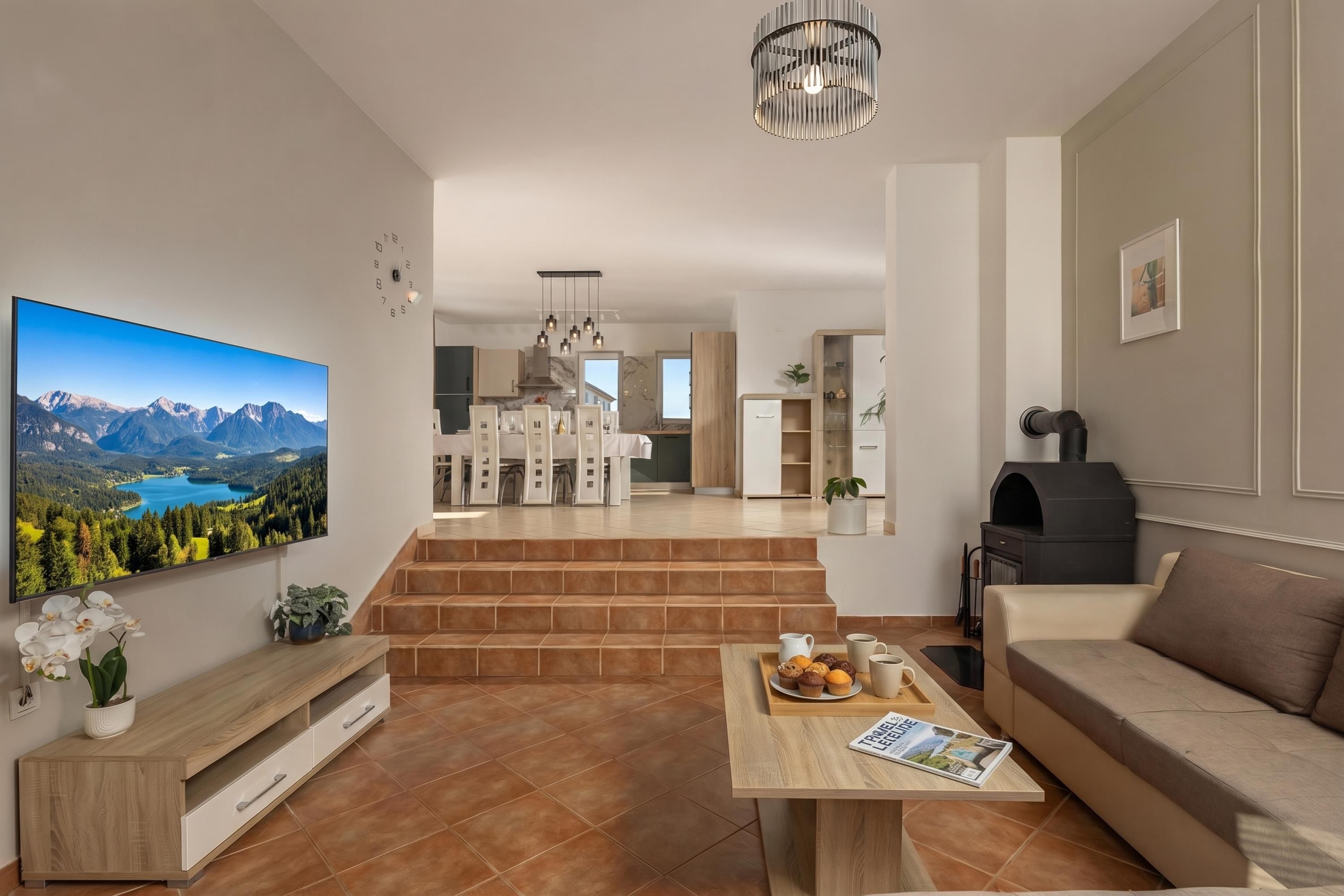A modern living room with a large flat-screen TV, a wooden coffee table with magazines, a sofa, and a fireplace.