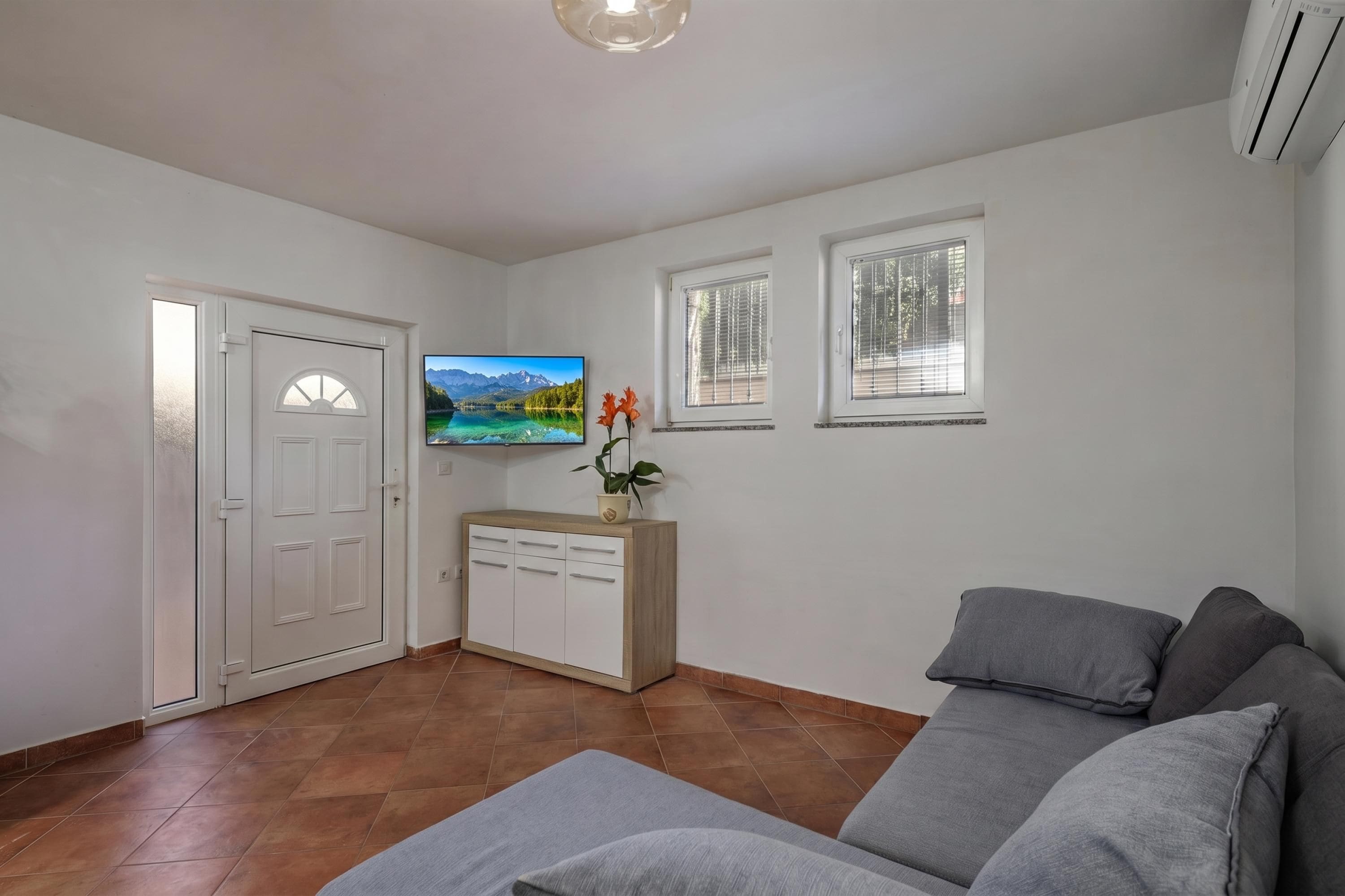 Un salon comprenant un canapé, un téléviseur fixé au mur, un meuble et une porte.