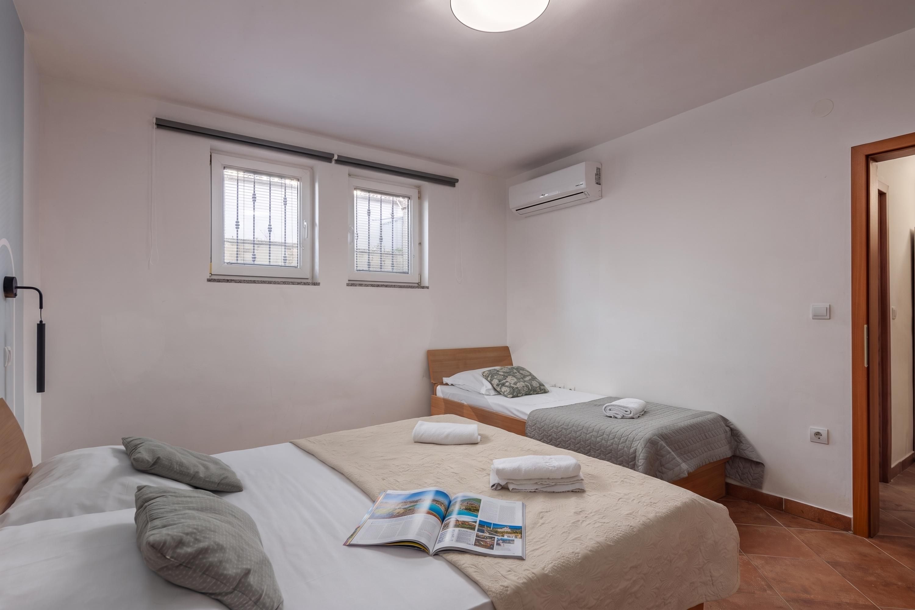 A bedroom with two beds, a window, an air conditioning unit, and a door.