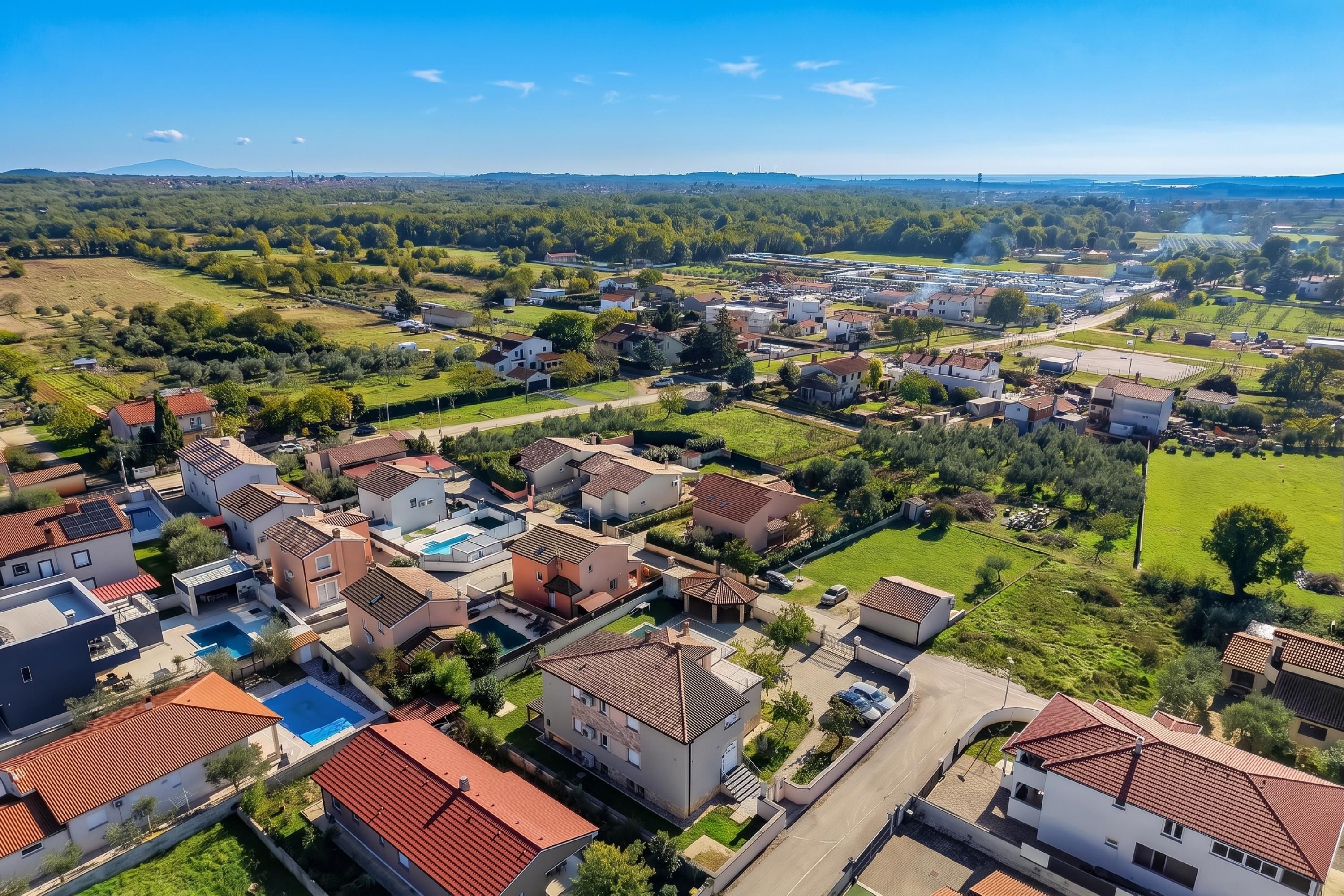 A residential area with houses, a swimming pool, and a large industrial complex in the background.