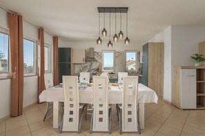 Een moderne keuken met een eethoek, met een marmeren spatwand, hangende lampen en uitzicht naar buiten.