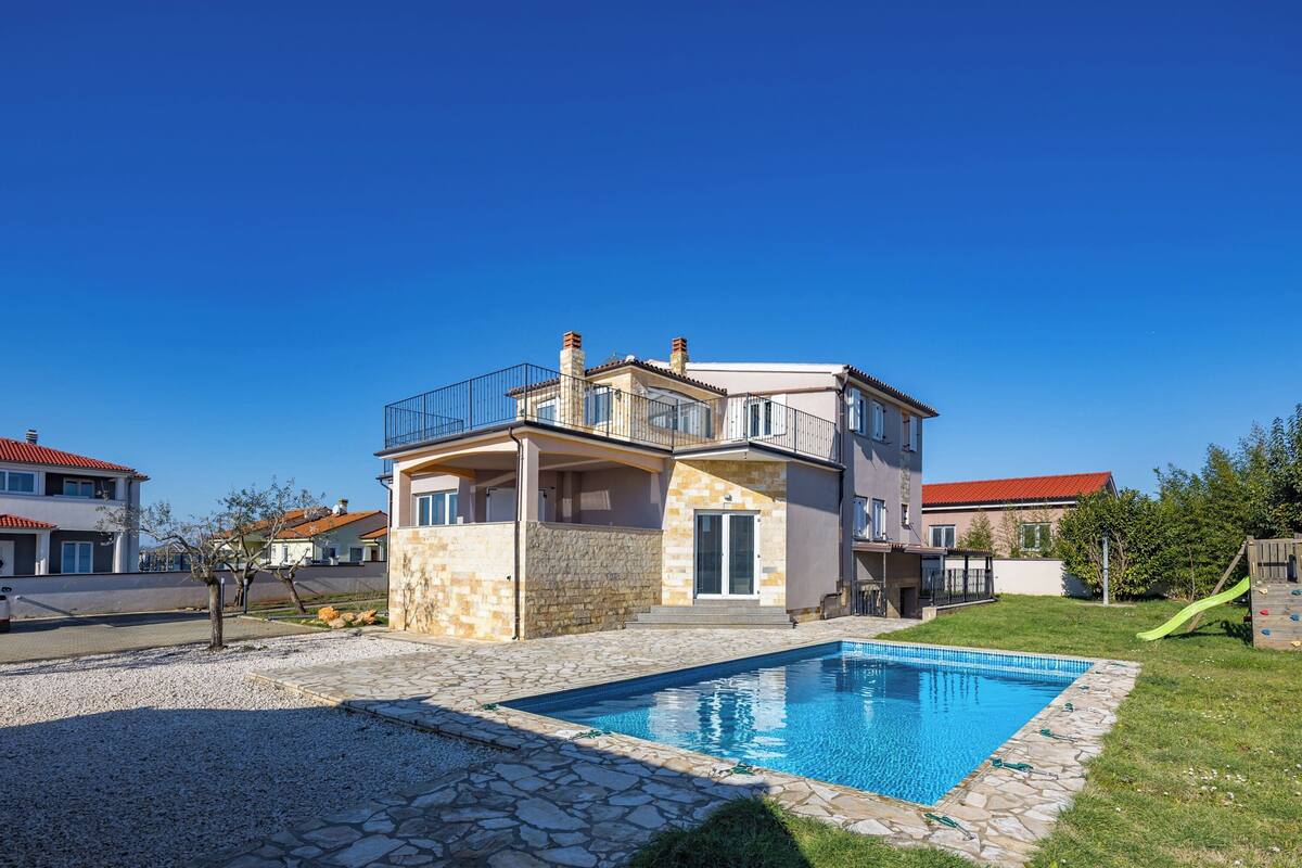 Ein zweistöckiges Haus mit Schwimmbad, Naturstein-Fassade und einem Balkon.