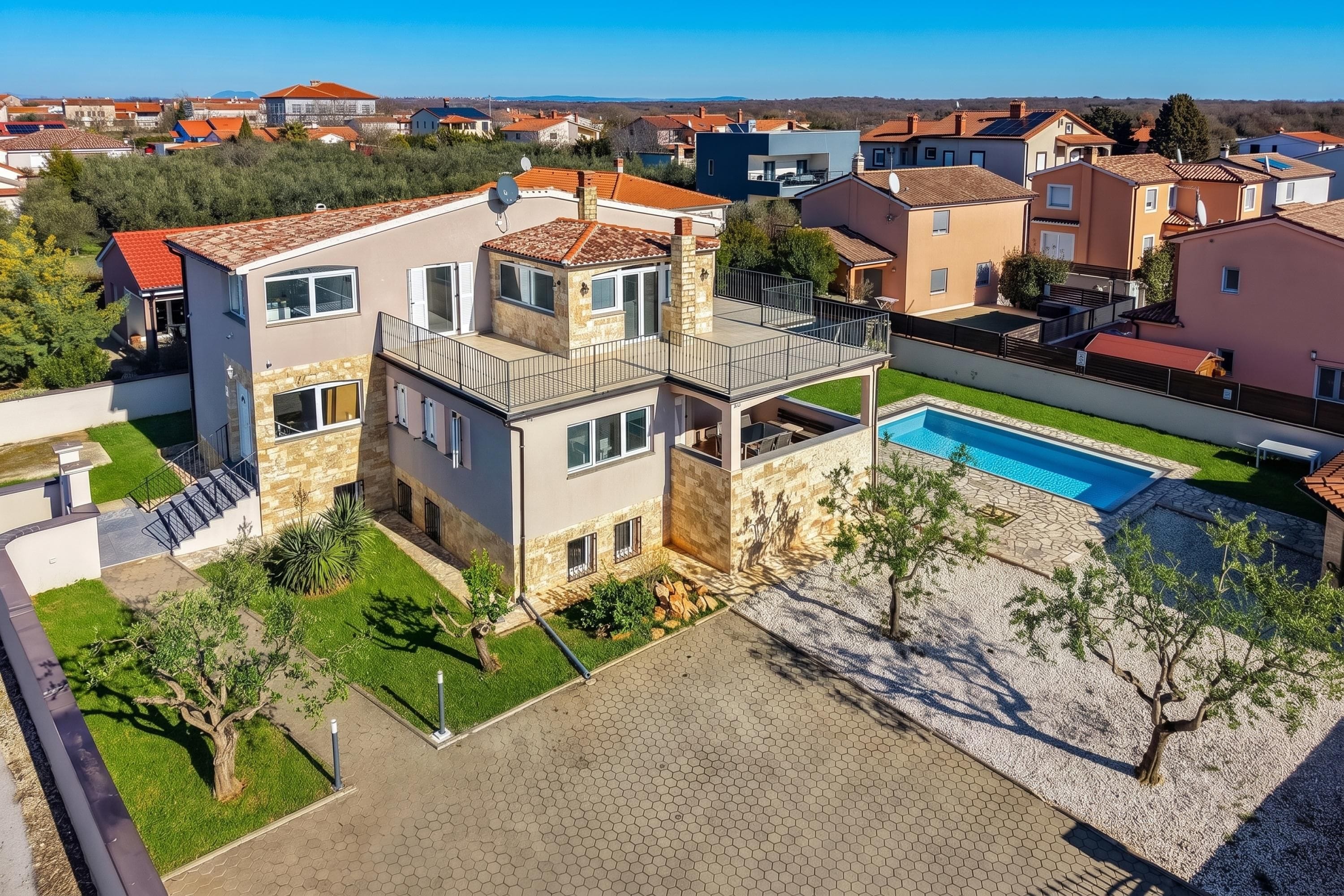 A modern two-story house with a swimming pool, surrounded by a well-maintained lawn and a paved driveway.