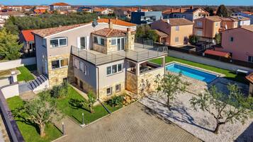 A modern two-story house with a swimming pool, surrounded by a well-maintained lawn and a paved driveway.