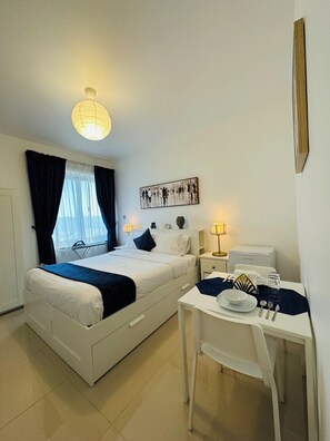 Ein Hotelzimmer mit einem Bett, einem Schreibtisch und einem Stuhl. Es gibt ein Fenster mit Vorhängen, ein Wandbild und eine Deckenleuchte.