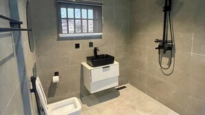 Un baño moderno con bañera, lavabo de cerámica negra, ventana y ducha con cabezal de ducha manual.