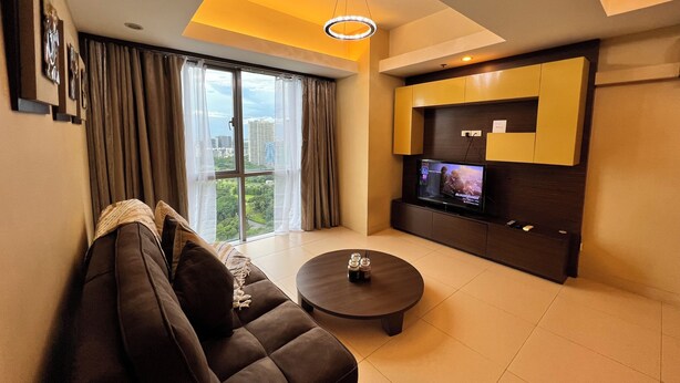 A modern living room with a sofa, a coffee table, and a TV mounted on a wall. - Comfort Meets Space: Large 1BR in Central BGC (Taguig)