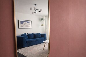 Une pièce avec un canapé bleu, un tableau encadré, un lustre moderne et une petite table blanche.