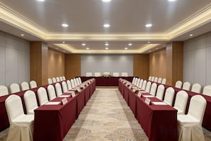Un salón de conferencias con una larga mesa, filas de sillas y suelo alfombrado.