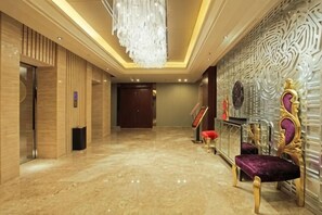 Un vestíbulo de hotel con suelo de mármol, una araña y un mostrador de recepción, además de una pared decorativa.